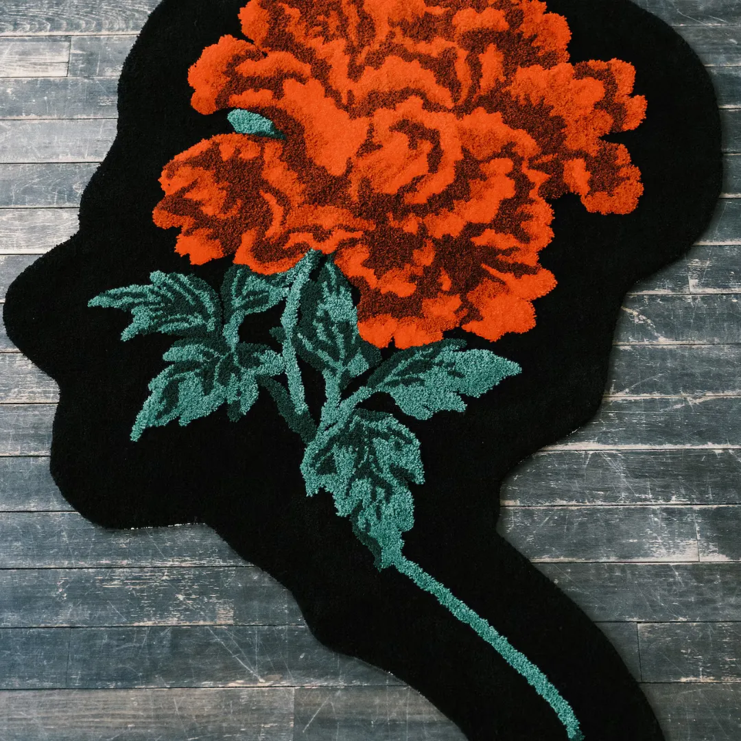 Black rug in the shape of a head silhouette with red blooming flower and green leaves, handmade for bold and thoughtful decor