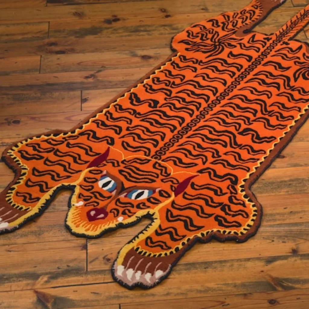 amber raja hand tufted tibetan tiger rug design Angled full-length view of the Amber Raja rug, highlighting the vibrant orange wool background and intricate black wandering stripe pattern characteristic of Tibetan folk art.