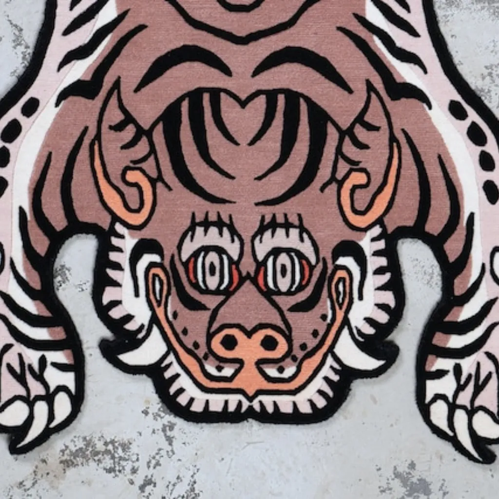 blush prowl pink tibetan tiger rug head detail Close-up top down view of the Blush Prowl Tibetan Rug, focusing on the stylized tiger face with striking teal eyes, sharp teeth, and black wavy stripes on a soft blush pink background.