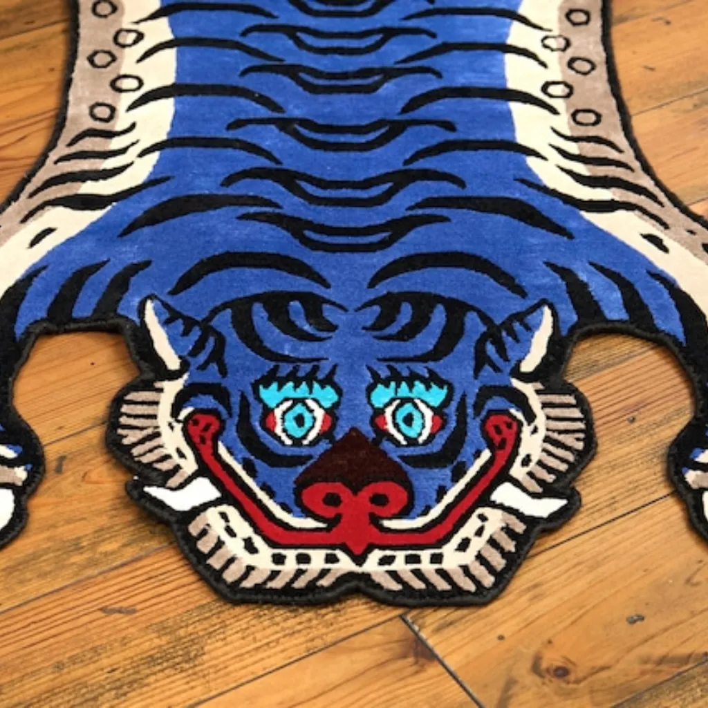 cobalt fang tibetan blue tiger rug head detail Close-up top down view of the Cobalt Fang Tibetan Rug, focusing on the stylized blue tiger face with vibrant teal eyes, red mouth, and black wavy stripes.