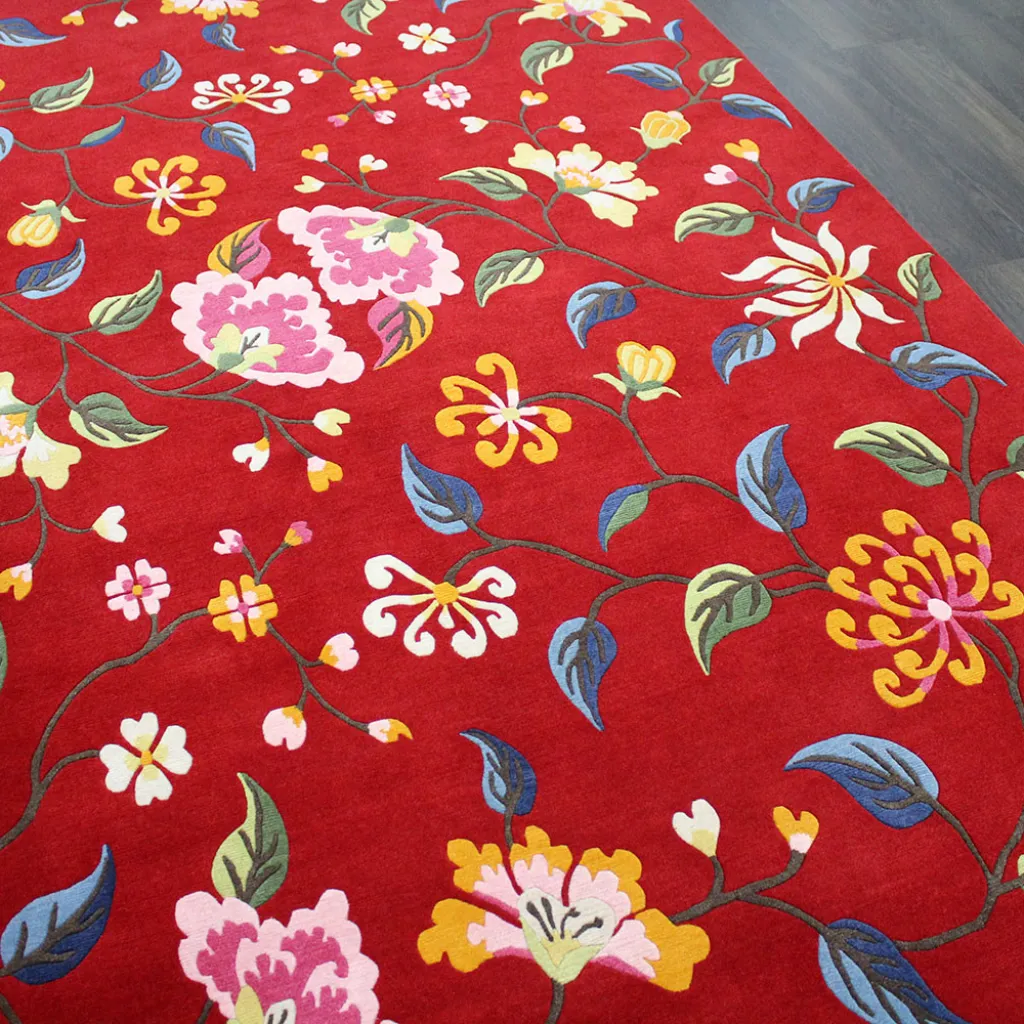 crimson valley floral pattern red rug Angled close up view of the Crimson Valley rug featuring intricate trailing vines with pink, yellow, and blue flowers on a vibrant red wool background.