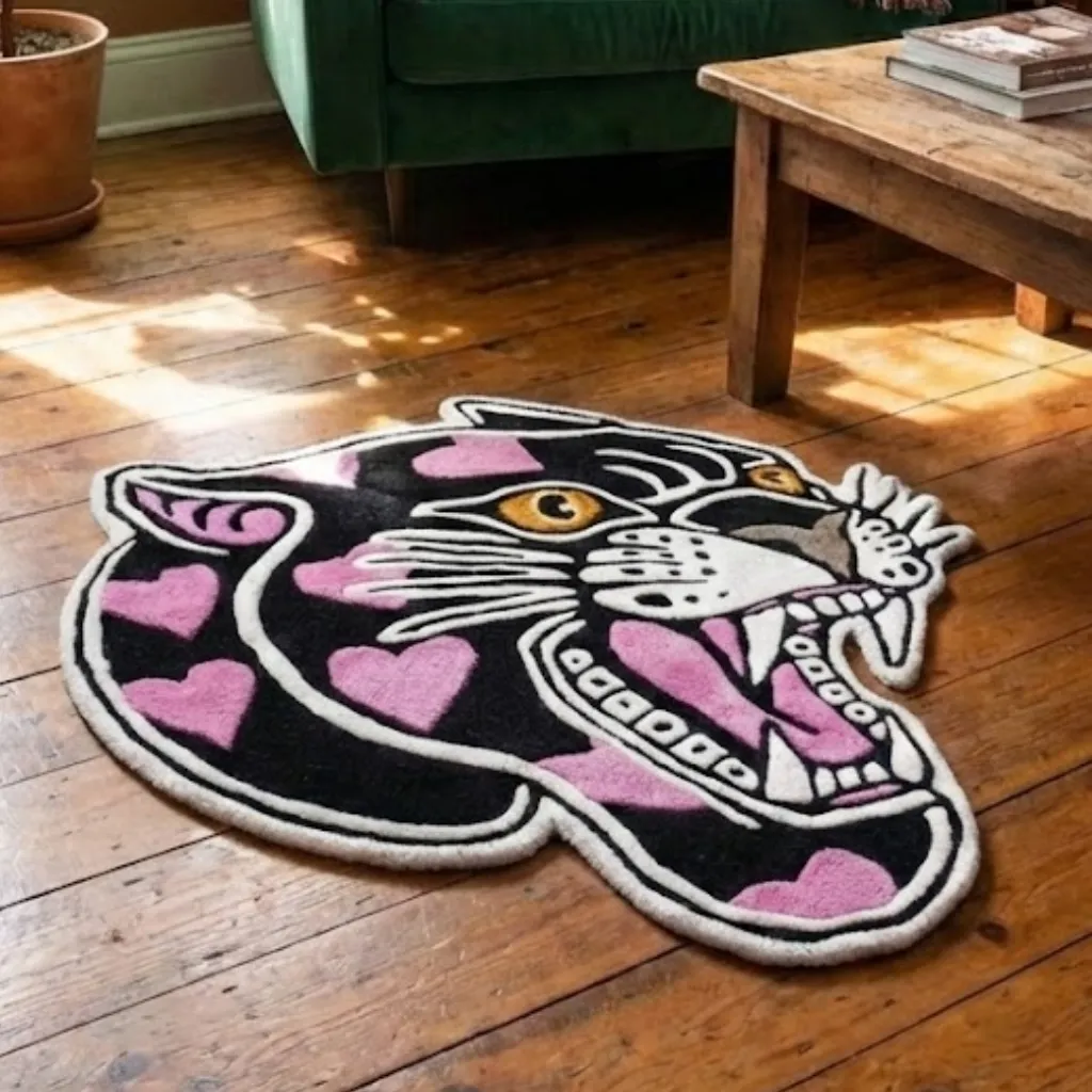 Hand Tufted Pink Panther Tattoo Rug On Wood Floor Angled view of the panther head rug with pink hearts lying on a wooden floor, highlighting the thick hand-tufted wool pile and custom die-cut shape.