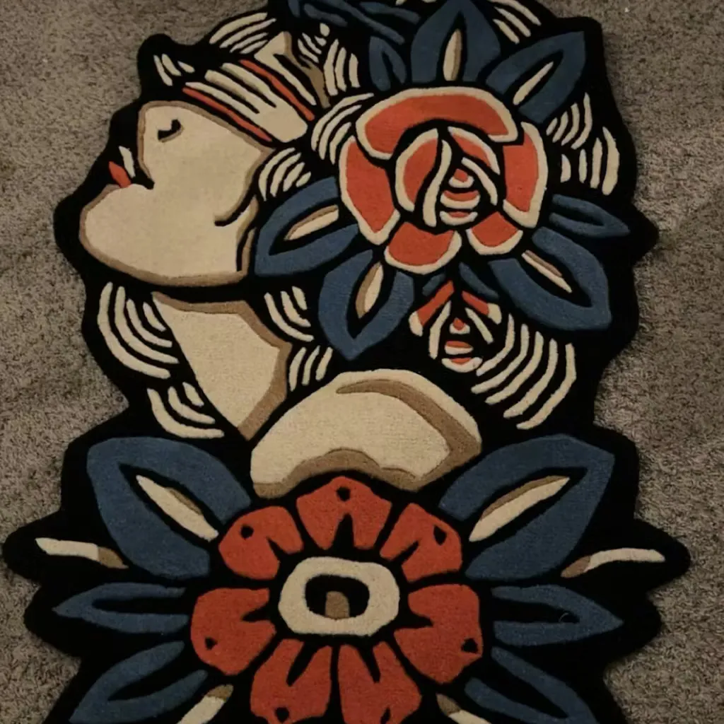 Hand Tufted Traditional Tattoo Art Rug Close up detail shot of the Lady Rose rug highlighting the dense hand tufted wool texture and the rich blue and orange hues of the floral motifs against a black background.