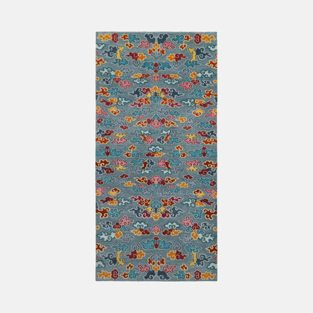nomad horizon blue tibetan style rug Top down full view of the Nomad Horizon rug featuring a traditional repeating pattern of stylized clouds in red, yellow, and pink on a soft blue background.