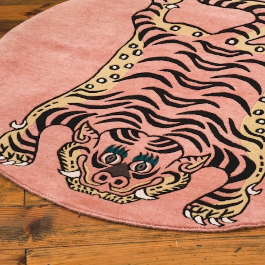 petal prawl hand tufted wool round rug design High angle view of the round Petal Prawl rug placed on a rustic wooden floor, featuring a traditional Tibetan tiger design adapted into a circular pink format with yellow accents.