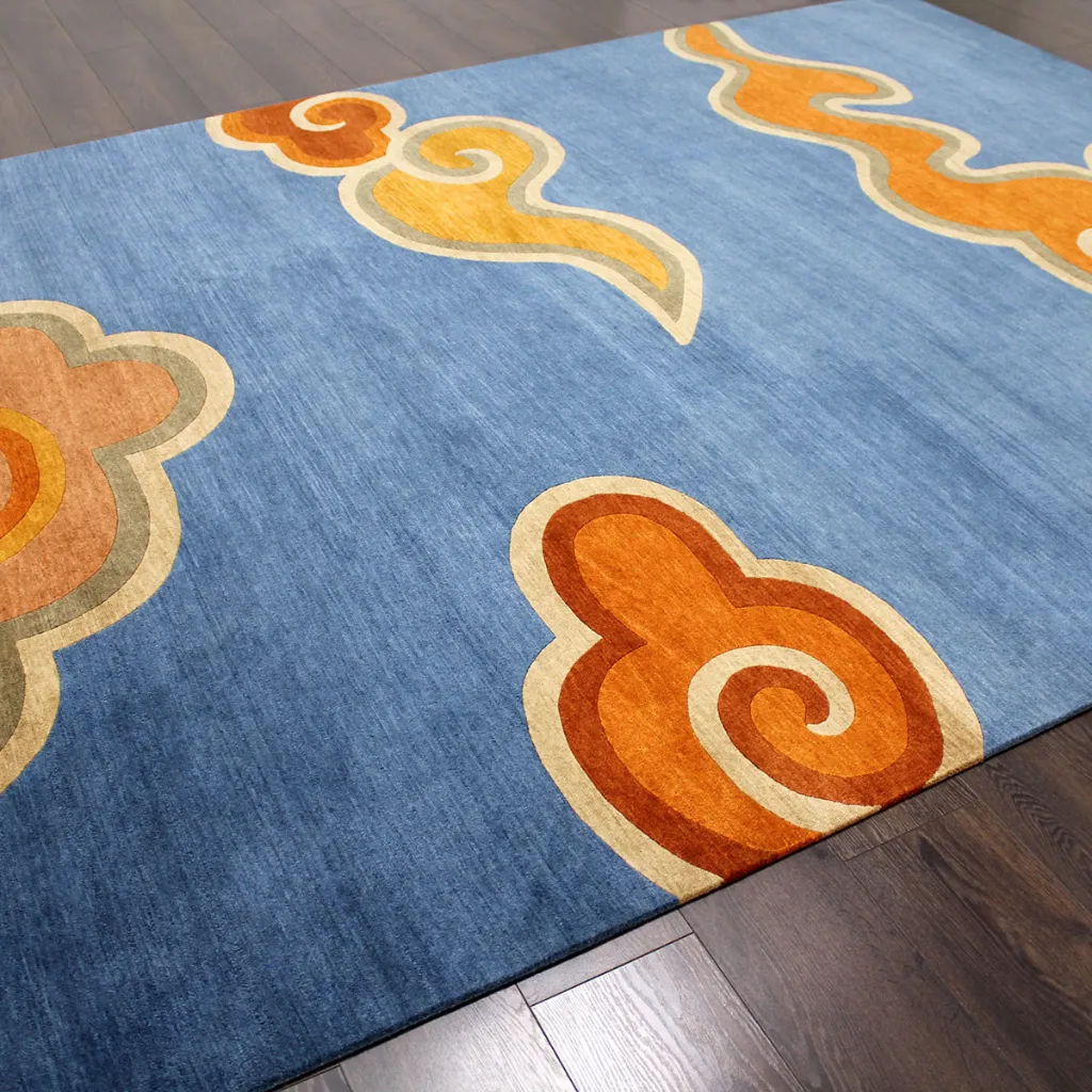 skybound weave hand tufted wool rug angled view Angled perspective of the Skybound Weave rug showing the soft blue wool background and the vibrant orange and yellow traditional cloud motifs.