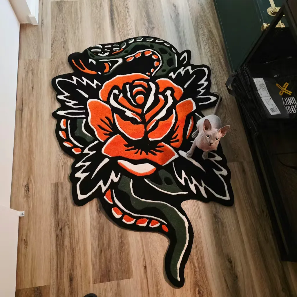Snake And Rose Shaped Floor Rug With Cat Top down lifestyle view of the Snake Rose rug with a cat sitting nearby, highlighting the intricate orange flower and green serpent design set against a black background.