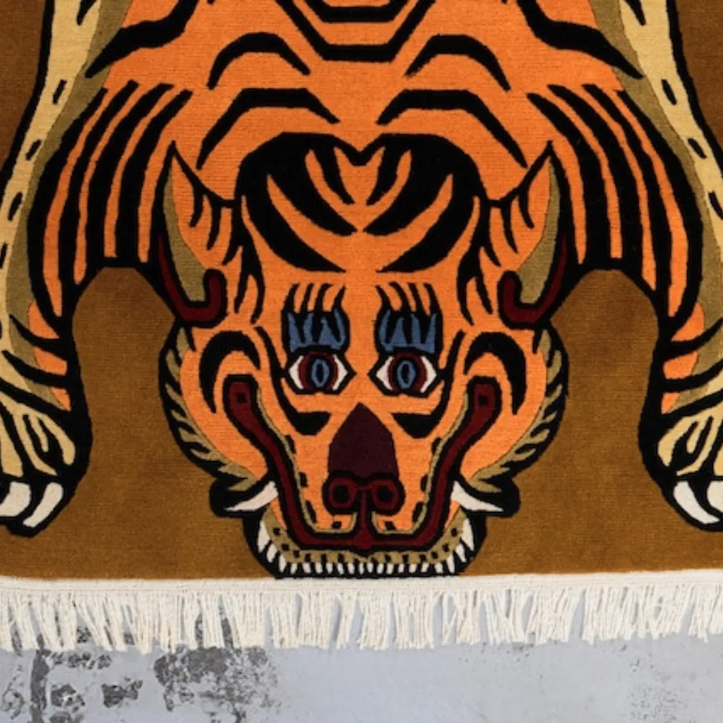sunstripe roar yellow tibetan tiger rug head detail Close-up top down view of the Sunstripe Roar Tibetan Rug, focusing on the stylized tiger face with bright blue eyes, red mouth details, and black wavy stripes on a warm mustard yellow background.