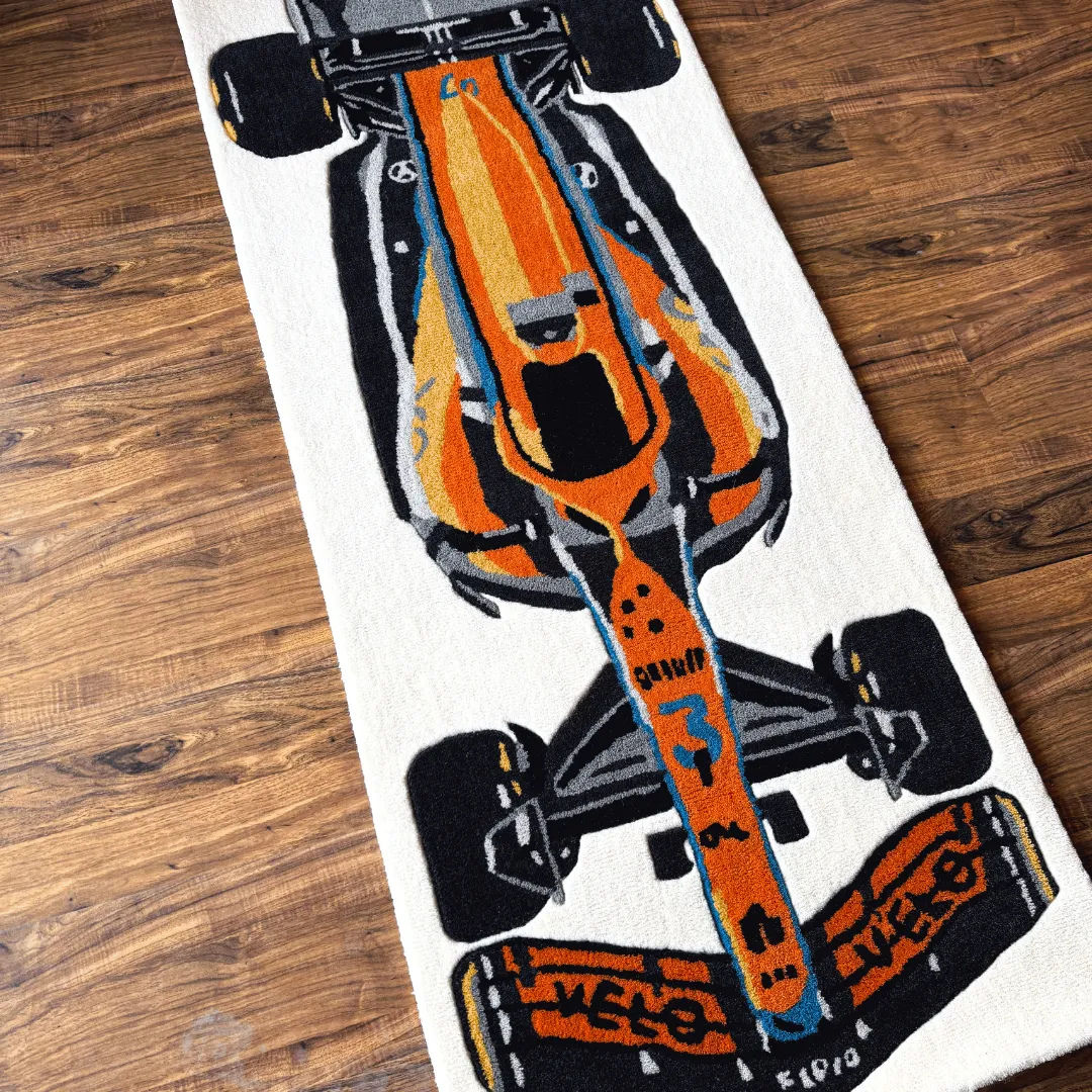 ignite rush f1 car wool rug detail Close-up top-down detail of the Ignite Rush rug, highlighting the vibrant orange and blue livery of the race car design and the plush hand-tufted wool texture.