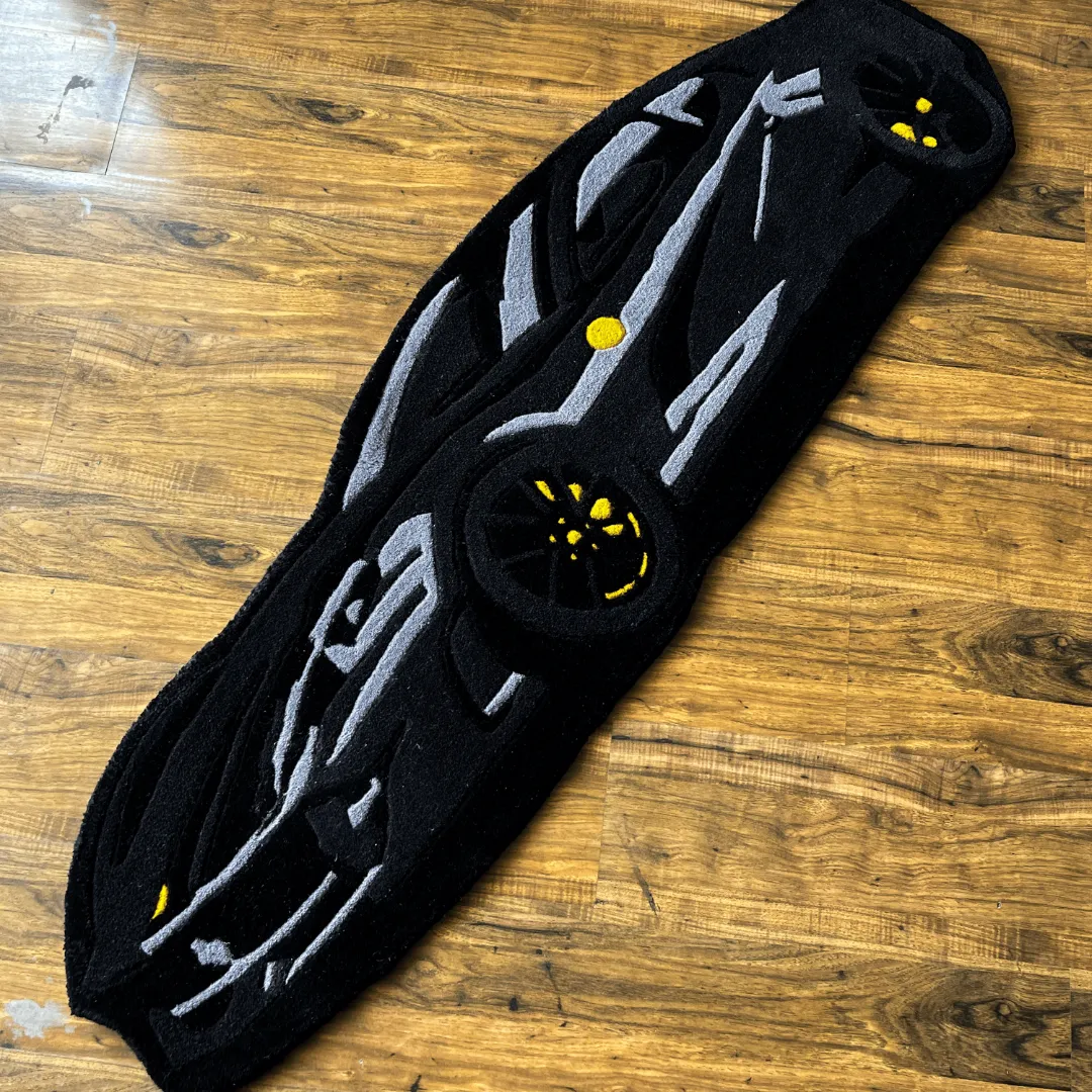 shadow monarch black sports car rug High angle view of the Shadow Monarch rug shaped like a sleek black sports car, featuring grey aerodynamic lines and vibrant yellow wheel accents.