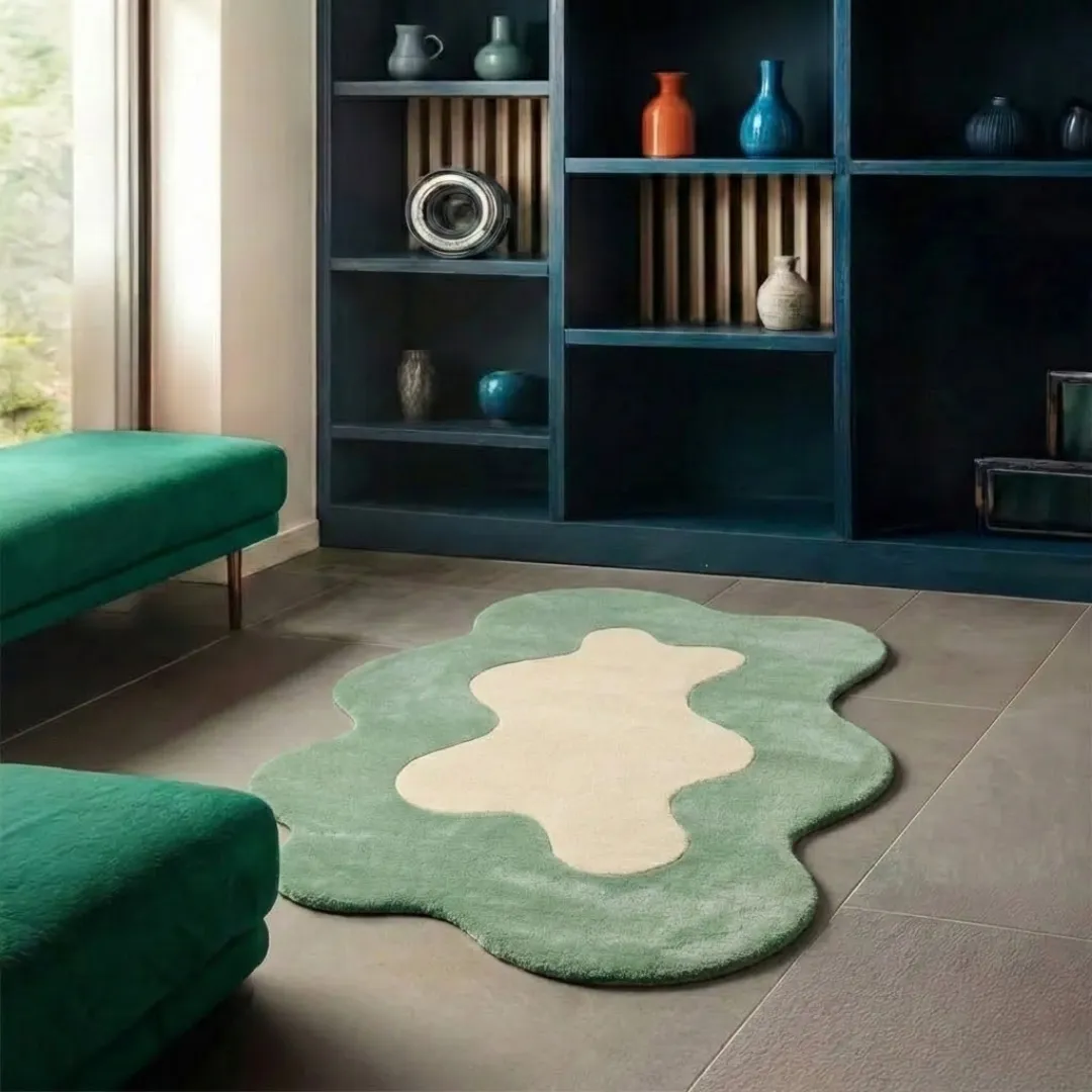 liom mist rug lifestyle Perspective lifestyle view of the Liom Mist rug placed on a grey tile floor, showcasing its unique wavy border and calming sage green and cream palette in a modern room styled with green velvet benches.