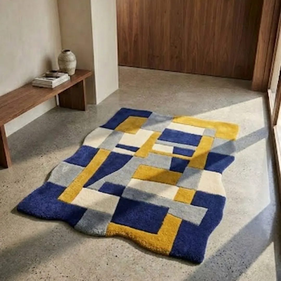 offset frame rug lifestyle Perspective lifestyle view of the Offset Frame rug placed on a polished concrete floor, showcasing its bold multi-colored geometric blocks and unique wavy border in a sunlit modern interior.