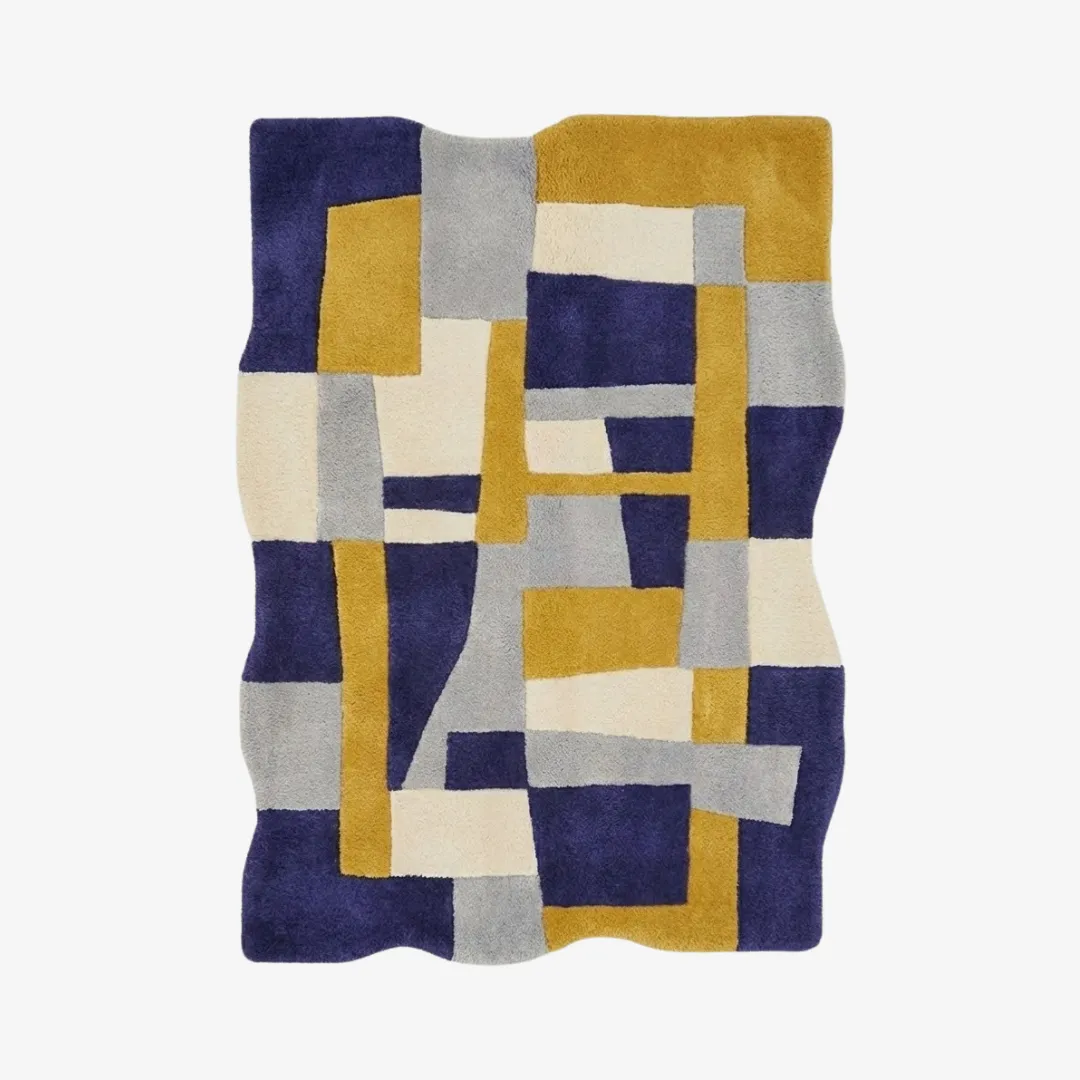 offset frame rug top A top-down view of the Offset Frame rug, featuring an irregular wavy silhouette and a geometric patchwork design composed of royal blue, mustard yellow, light grey, and cream rectangular blocks.