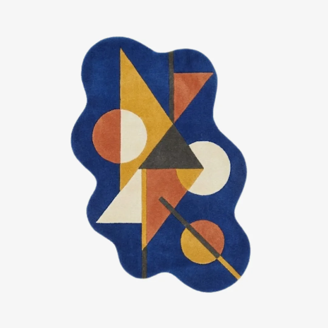 prisma axis rug top Top-down view of the Prisma Axis rug featuring a fluid, wavy silhouette and a vibrant geometric design of triangles and circles in yellow, orange, and cream on a royal blue base.
