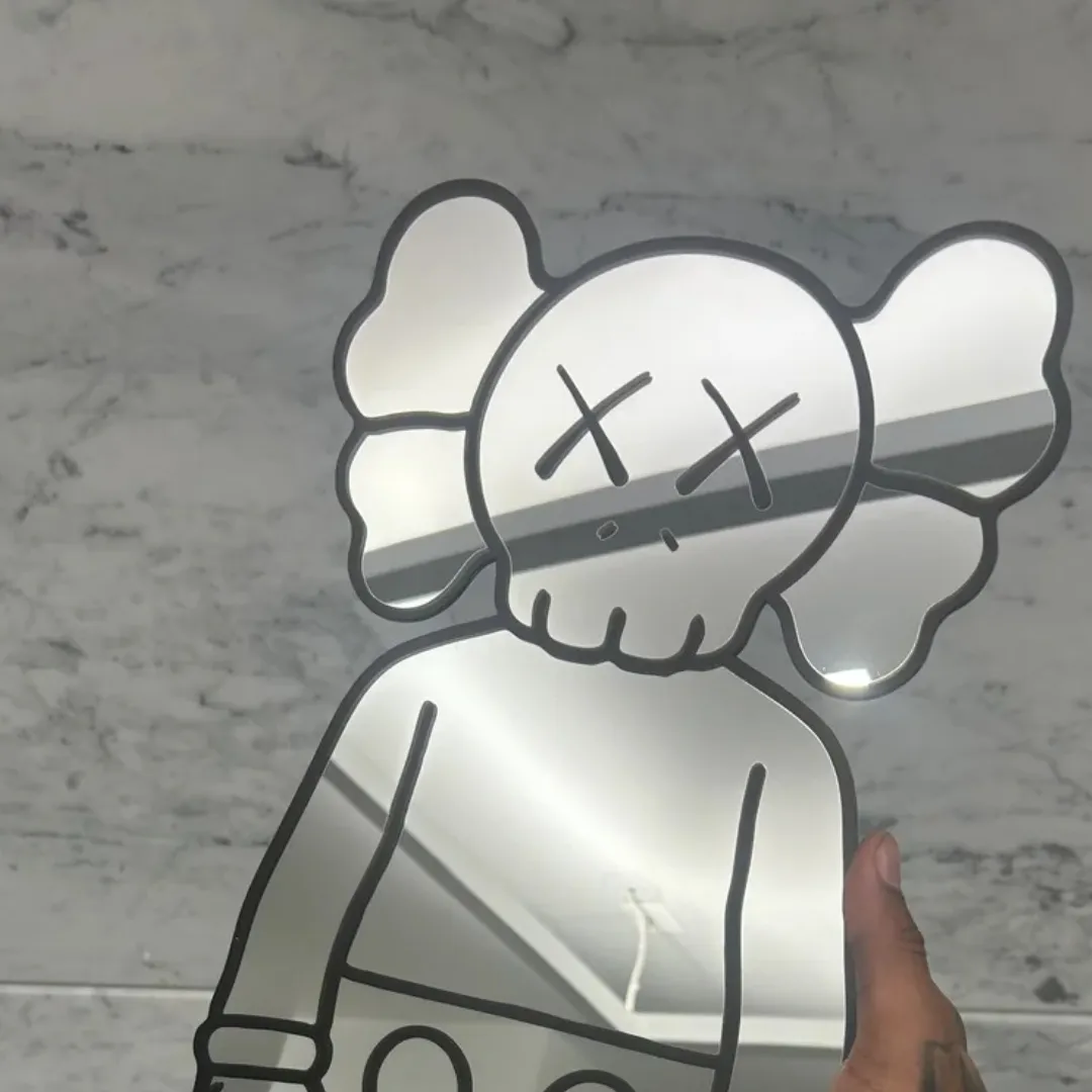 street bear mirror close up hand held Close-up view of a hand holding the Street Bear mirror against a marble wall, highlighting the character's distinctive X-eyes and skull-like face design while reflecting the room's ceiling.