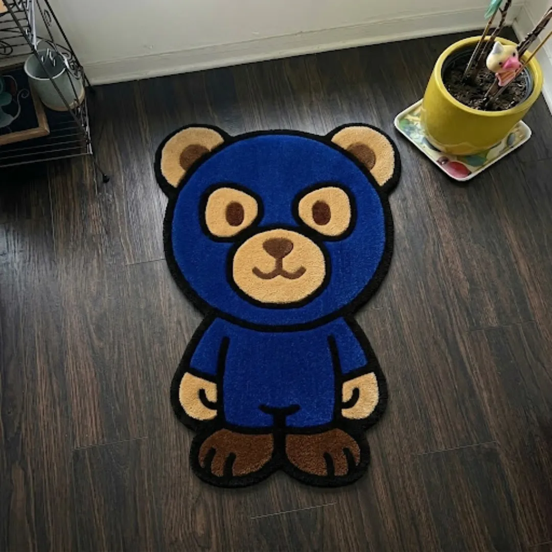 liberty shield shaped area rug product shot A top-down studio product photograph of a unique, character-shaped area rug featuring a blue bear design with brown accents, displayed on a dark wooden floor.