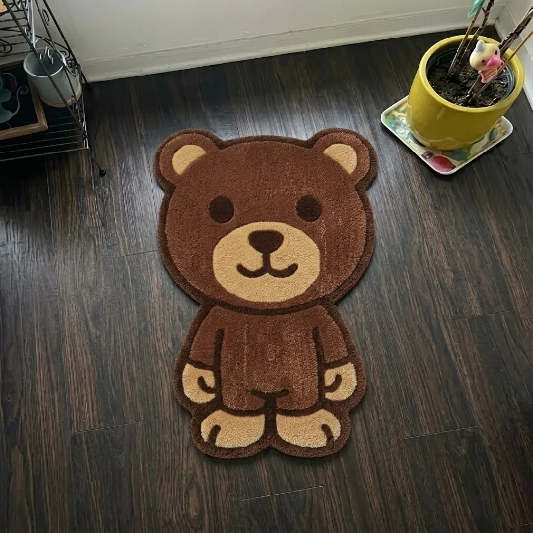webstrike phantom shaped area rug product shot A top-down studio product photograph of a unique, character-shaped area rug featuring a cute brown teddy bear design, displayed on a dark wooden floor.